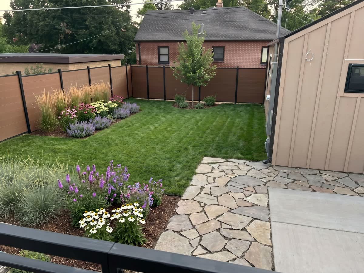 The same backyard fully replanted: new lawn, mulched beds of grasses, coneflowers, liatris, and catmint, a flagstone path, and a young tree