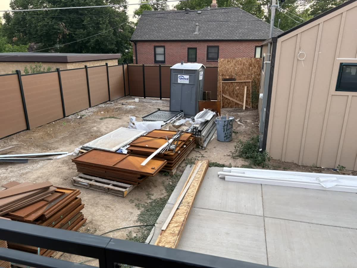 A Denver backyard mid-construction: bare dirt, stacked lumber, a plain fence